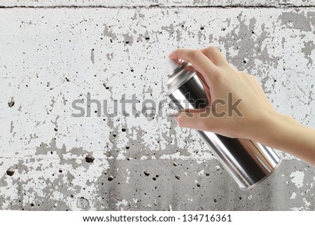 Human hand holding a graffiti Spray can in front of blank concrete wall