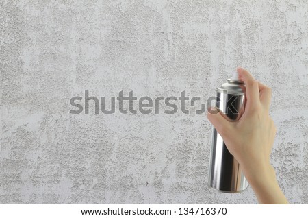 Human hand holding a graffiti Spray can in front of blank concrete wall