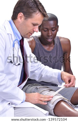 Male medical doctor secures leg brace on young black male athlete on white background