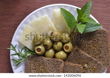 Plate of assorted healthy Mediterranean diet snacks including cheese, bread, stuffed olives, rosemary, and mint leaves with olive oil