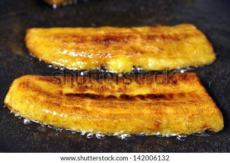 Closeup of crisp yellow sliced plantain bananas frying in pan with hot oil