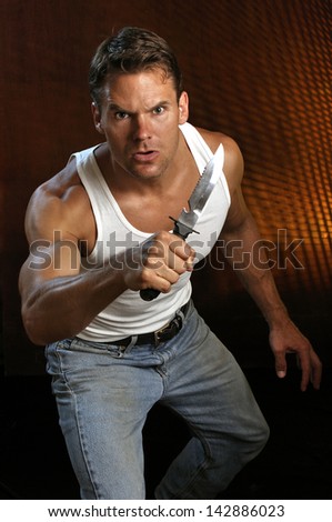 Muscular Caucasian man yielding a large survival knife prepares to attack
