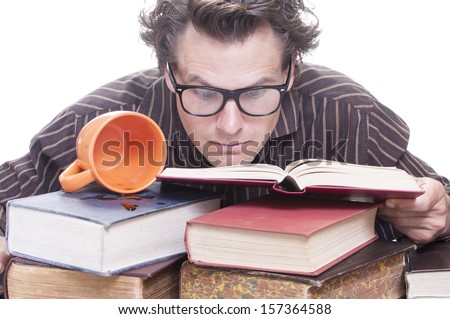 Young wide-eyed studious male Caucasian student studies intensely as he buries his eyes into pile of books next to spilled cup of coffee on white background