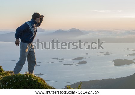 Caucasian male hiker on top of mountain looks out over Sitka Sound during summer sunset on Baranof Island in southeast Alaska