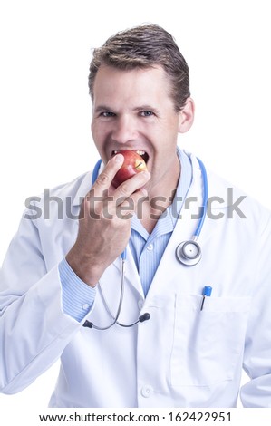 Handsome young medical doctor takes a bite into a red apple as a positive example of good health on white background