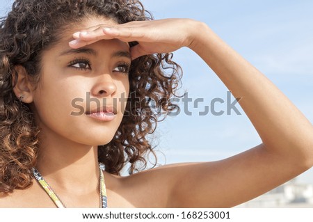 Beautiful young surfer girl shields eyes from sun as she observes the scene