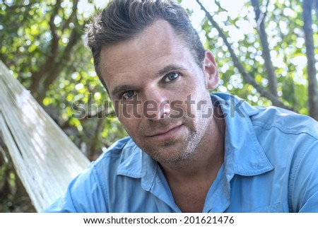 Portrait of handsome rugged adventurous man sitting in hammock in wilderness