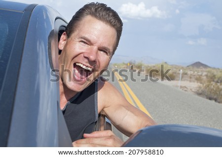 Closeup of handsome free Caucasian man driving car with head out window down desert road as he laughs with extreme excitement