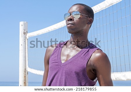 Handsome young African American man looking cool and styling in shades and tank top by volley ball net at beach in summer