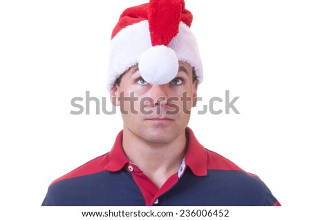 Caucasian man with confused expression in casual polo shirt looks up at white ball hanging between his eyes from red Santa hat on white background