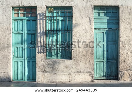 Two aqua green painted wooden doors and window of rustic exterior of old colonial style building illuminated by morning light in Merida, Yucatan, Mexico