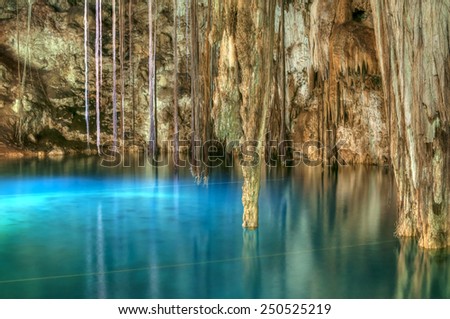 Beautiful clear blue water of Xkenken cenote in Dzitnup, Mexico illuminated from above with tree roots and stalactites hanging from ceiling of cavern