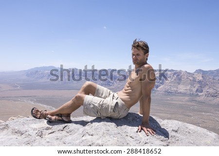 Muscular shirtless Caucasian man wearing shorts and sandals rests on top of mountain peak after a successful climb in Red Rock Canyon, Nevada