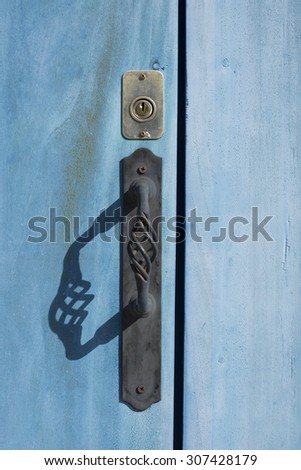 Closeup and shadow of black iron door handle and brass key lock on exterior of blue wooden door in Valladolid, Mexico