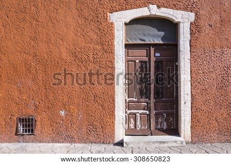 Unique textured red wall and colonial-style rustic entry door in historical Mexican town of Valladolid with copy space for text