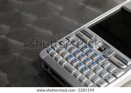 A silver colored pocket email and phone gadget showing screen and miniature keyboard lying on a metal tabletop