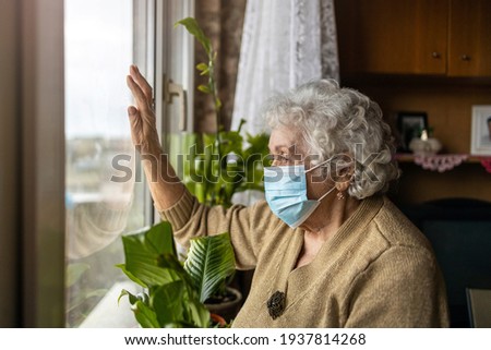 Senior woman with face mask looking out of window at home
 Stock foto © 