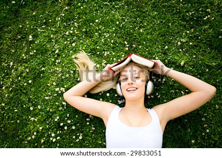 Woman lying on grass with book and headphones