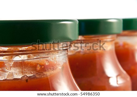 Close and low level angle capturing the top portions of a line of clear jars containing pasta sauce. First jar in focus.
