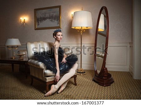 Ballerina in black tutu sitting in armchair in front of mirror