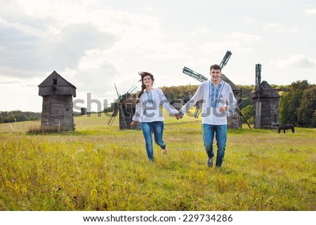 Happy young couple running on the field, against some old mills in the background