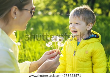 Cute toddler boy making a with before blowing dried dandelions in mother\'s hands
