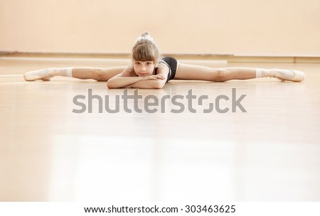 Young girl doing splits while warming up at ballet dance class