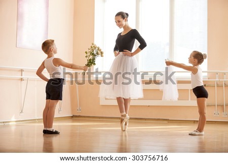 At ballet dancing class: young boy and girl giving flowers and veil to older student while she is dancing en pointe