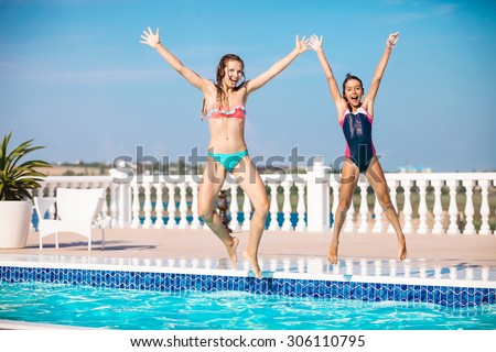 Young mother and daughter jumping into the swimming pool and screaming of joy