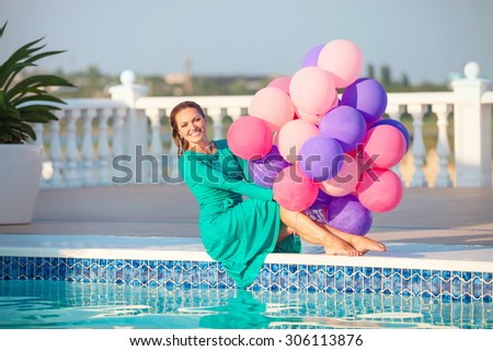 Happy young woman with a bunch of balloons after jumping into a swimming pool in a dress
