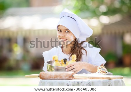 Smiling little chef showing ducklings in a bowl while cooking outdoors