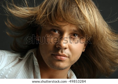 Portrait of young handsome man on black background with hair fluttering in wind, studio shot