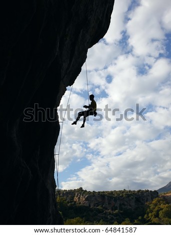 Silhouette of rock climber going down after reaching the top of the route with cloudy sky background