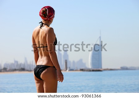 Rear view of young woman on Jumeira beach, with famous luxurious Burj Al Arab Hotel in distance, Dubai, UAE
