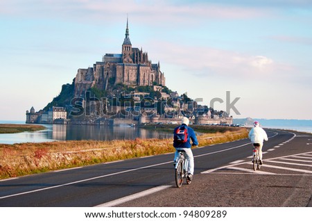 MONT SAINT-MICHEL, NORMANDY, FRANCE - SEPTEMBER 18: Mont Saint-Michel, a rocky island in Normandy, France, is the seat of the Saint-Michel monastery. Two senior people cycling towards the monastery, on Sept 18, 2005.
