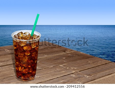 Cola in takeaway cup on wooden table by the sea
