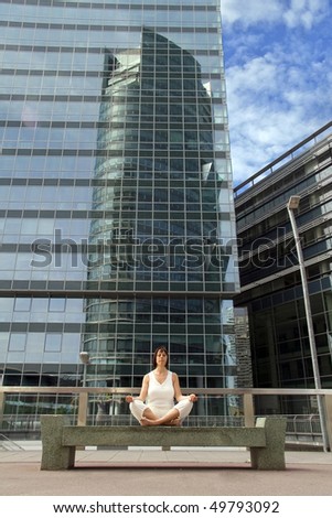 a white woman is exercising yoga and meditation in front of a modern office building.