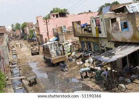 a road in an indian slum in agra, at the end of the road you see the dome of the monumental landmark Taj Mahal which symbolize the contrast of poverty and wealth.