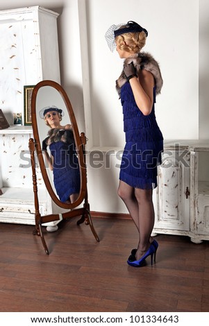 A beautiful young girl dressed in the style of 1920\'s, looking at herself in the mirror