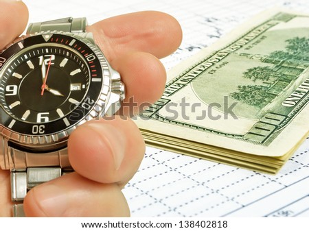 The hand with the clock on the background of the exchange graph with a pack of dollars.