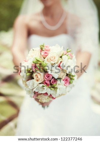 Bride in a white dress in summer green park with a bouquet in hand