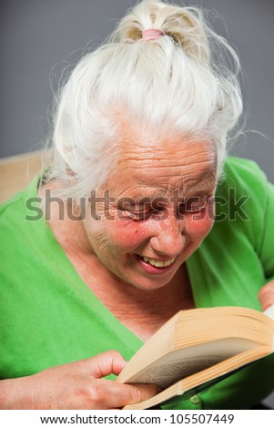 Senior woman sitting chair reading a book. Grey long hair. Studio shot isolated on grey background.