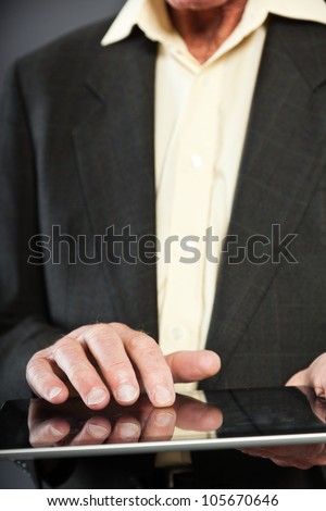 Closeup of hand from senior man in dark suit against grey wall. Using tablet. Well dressed. Studio shot.