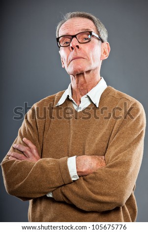 Expressive good looking senior man wearing glasses against grey wall. Funny and characteristic. Well dressed. Studio shot.