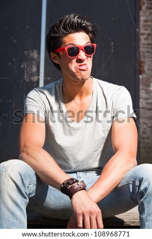 Urban asian man with red sunglasses making funny face. Good looking. Cool guy. Wearing grey shirt and jeans.