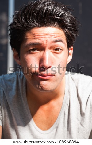 Urban asian man making funny face. Good looking. Cool guy. Wearing grey shirt.
