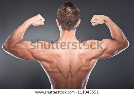 Shirtless muscled fitness man showing his back. Cool looking. Tough guy. Blue eyes. Blond short hair. Wearing black sunglasses. Tanned skin. Studio shot isolated on grey background.