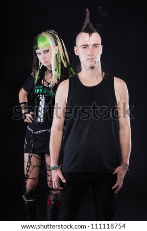 Couple of cyber punk girl with green blond hair and punk man with mohawk haircut. Expressive faces. Smoking cigarette. Isolated on black background. Studio shot.