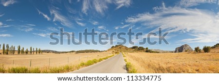 Beautiful panoramic photo of road through Sierra de Grazalema Natural Park. On the road. Blue cloudy sky. Golden fields with cypresses and rocks. Amazing scenery. Andalusia. Spain.