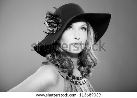 Glamour vintage black and white portrait of pretty woman with long hair. Wearing black hat with flower. Studio portrait isolated on grey.